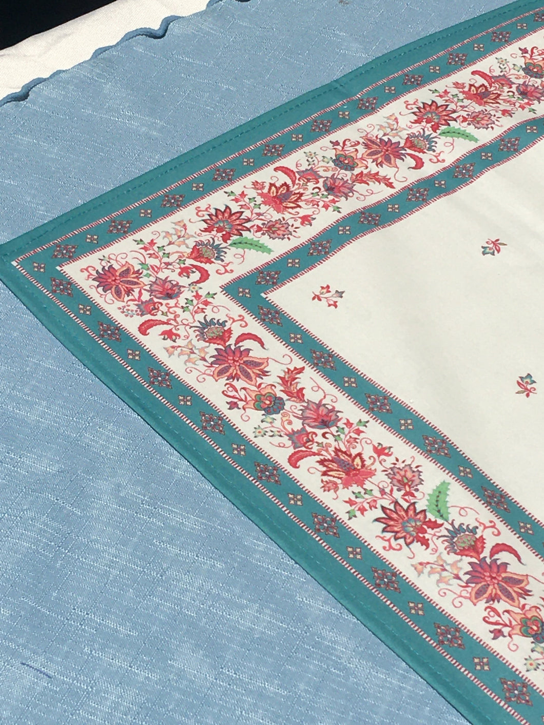 Anti stain wipe clean finish allows for liquids and oils to bead off. Measures 16.5 by 60 in. Pictured on a 72 inch length table for reference, but may be draped over the sides of a smaller table as well. Border color is blue turquoise and background is white eggshell with multicolor provincial flora.