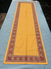 Load image into Gallery viewer, Acrylic coating allows for universal wipe clean finish, allowing for liquids and oils to bead off. Measures 16.5 by 60 in. Pictured on a 72 inch length table for reference, but may be draped over the sides of a smaller table as well. Manufactured by l'Ensoillade and made in France. Pictured in safran yellow with deep red accents.