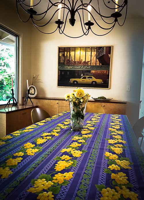 This acrylic coated cotton rectangular blue tablecloth measuring 97 inches in length celebrates vineyards and spring, with a beautiful motif of yellow grape clusters and leaves. Le Cluny, made in France. Easy care wipe clean finish. 